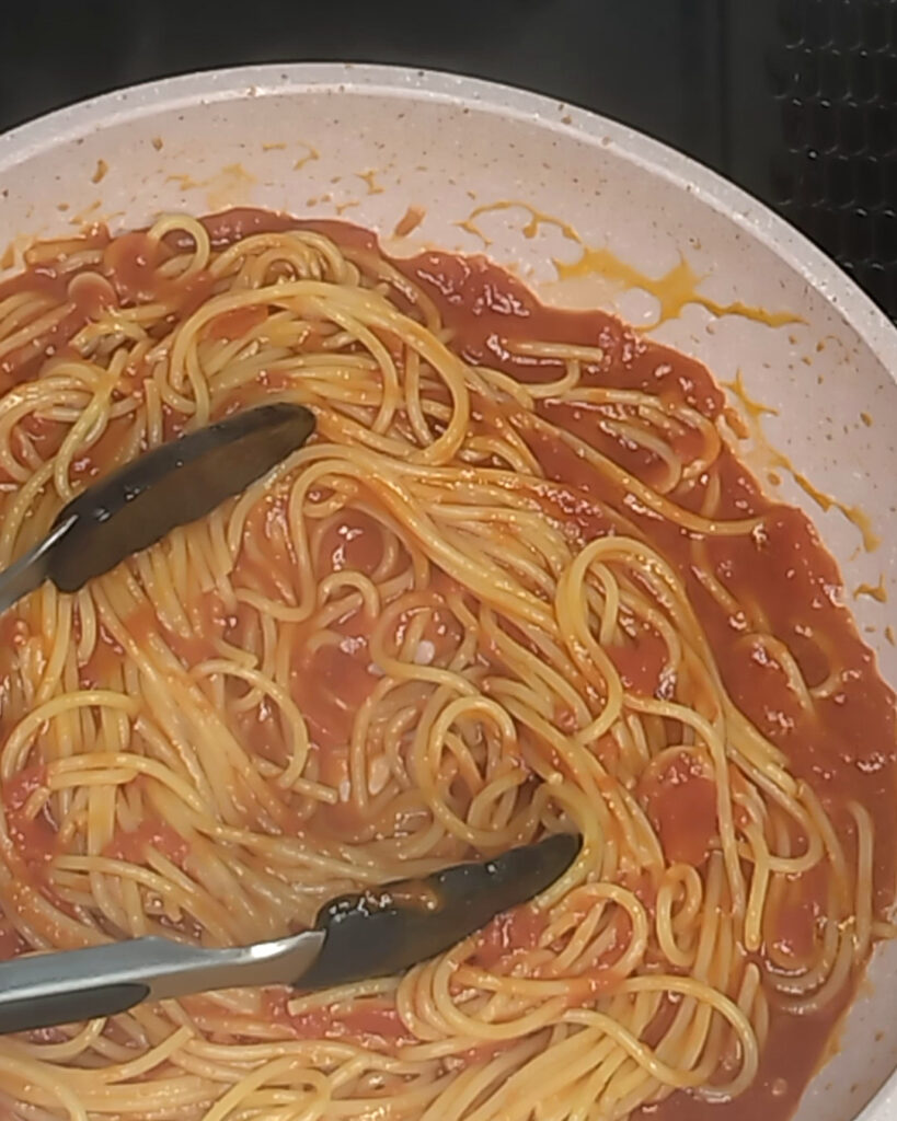 茹で上げたスパゲティを、トングでトマトソースと和えているところ